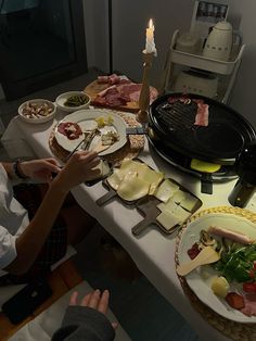 a person sitting at a table with food on it and a lit candle in the background