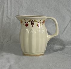 a cream colored ceramic pitcher with red flowers on the rim and gold trimmings