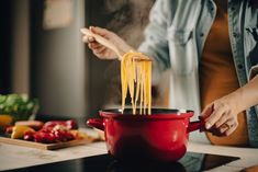 a woman is stirring spaghetti into a red pot