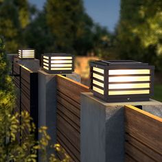 three lights on the side of a wooden fence in front of some bushes and trees