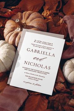 a white wedding card surrounded by autumn leaves and pumpkins with the words, garbiela and nicholas written on it