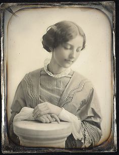 an old black and white photo of a woman with her hands resting on a urn