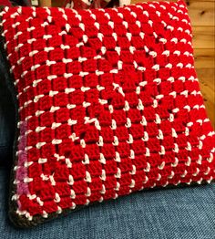 a red and white crocheted pillow sitting on top of a blue couch