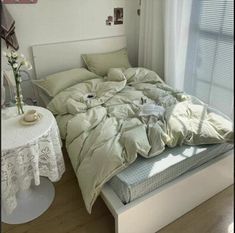 an unmade bed sitting next to a window in a room with white walls and wooden floors