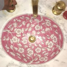 a bathroom sink with pink and white flowers on the bowl, gold faucet