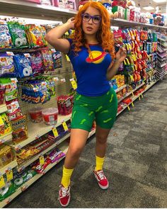 a woman with red hair wearing green shorts and a superman t - shirt in a grocery store