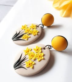 two yellow and white earrings with flowers painted on the front, one has an egg in the back