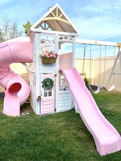 a pink slide in the grass next to a small house with a flower pot on top