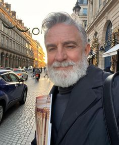 a man with a white beard and gray hair holding a book in his right hand