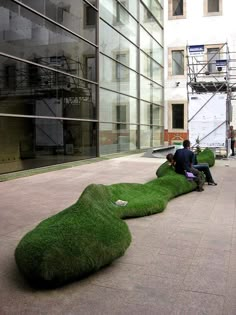 two people sitting on the ground in front of a building with grass growing out of it