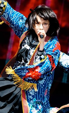 a woman in a colorful outfit holding a microphone up to her mouth while performing on stage