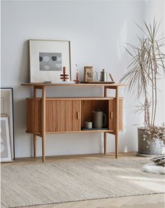 a living room with a wooden cabinet next to a potted plant and pictures on the wall