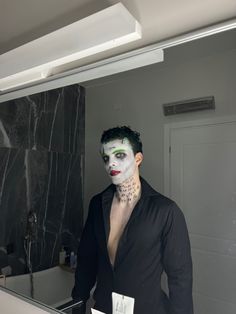 a man with white makeup and green eyes stands in front of a mirror wearing a black suit