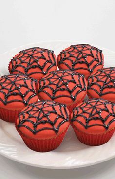 some red cupcakes with black icing on a white plate and spider web decorations