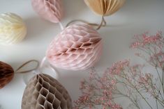 some paper balls and flowers on a white table with pink flowers in the background,