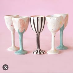 three wine glasses sitting next to each other on a pink surface with white and black stripes