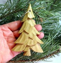 a hand holding a wooden ornament shaped like a christmas tree on a pine branch