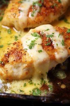 two pieces of chicken covered in cheese and parsley on top of a skillet