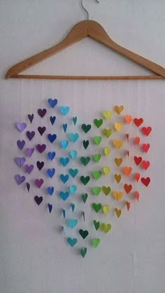 multicolored paper hearts hanging from a wooden hanger on a white wall next to a coat rack