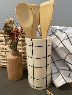 three wooden spoons in a cup next to a basket with flowers and other kitchen utensils