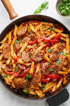 a skillet filled with pasta and meat covered in marinara sauce, garnished with fresh basil