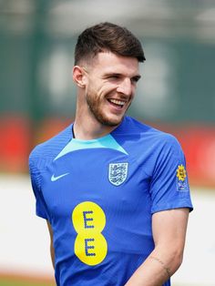 a man with a goatee smiles while wearing a blue shirt and holding a soccer ball