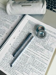 an open notebook with two rings on it next to a pen and a laptop computer