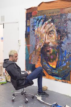 a man sitting in a chair next to a large painting