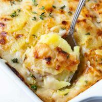 a close up of a casserole in a white dish with a serving spoon