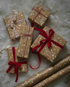 four wrapped presents with red ribbons and bows on a white furnishing area next to two candles