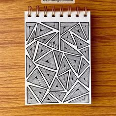 a spiral notebook with black and white designs on the cover, sitting on top of a wooden