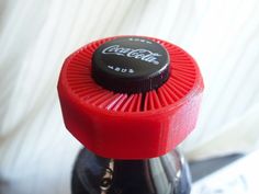 a coca - cola bottle cap sitting on top of a blender in front of a white curtain