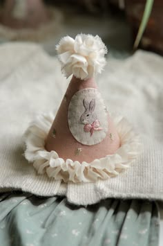 a small pink hat with a bunny on it's side sitting on top of a white blanket