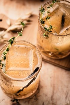 two glasses filled with ice and water on top of a wooden table next to spoons