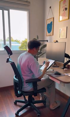 a person sitting at a desk in front of a computer monitor and writing on a piece of paper