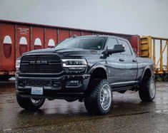 a black ram truck parked in front of a train car on a rainy day with its lights on