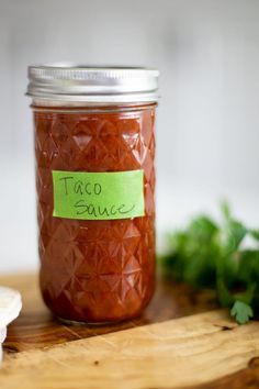 a jar filled with taco sauce sitting on top of a wooden cutting board next to parsley