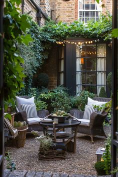 an outdoor seating area with potted plants and lights on the windowsill, surrounded by greenery