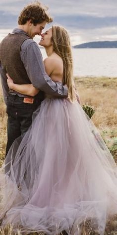 a man and woman standing next to each other in a field with water behind them