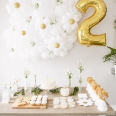 a table topped with lots of white and gold balloons next to a number two sign