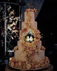 a three tiered wedding cake decorated with flowers and two birds on the top layer