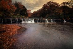 there is a large waterfall in the middle of the river with fall foliage around it