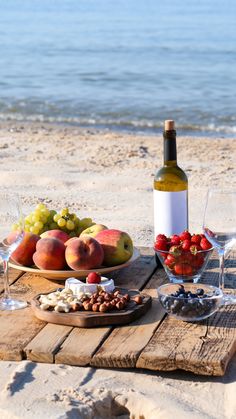 a table with wine, fruit and nuts on it at the beach near the ocean