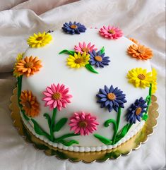 a cake decorated with colorful flowers on top of a white sheet covered tablecloth and gold trimmings