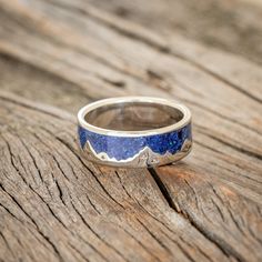 a silver ring with blue and white stone in the middle on top of a wooden table