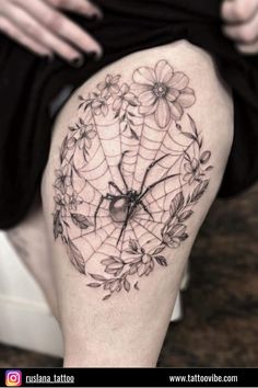 a woman's thigh with a spider and flowers tattoo on her leg, while she is sitting down