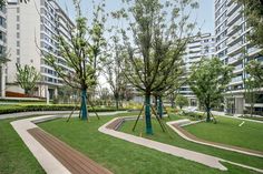 a park with trees, benches and sculptures in front of apartment buildings on a sunny day