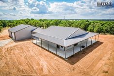 an aerial view of two metal buildings in the middle of a dirt field with trees