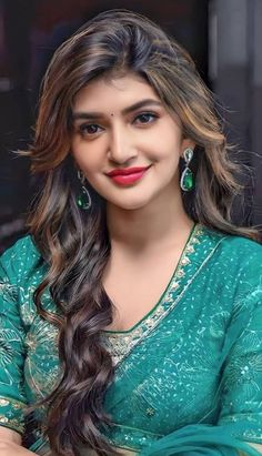 a woman with long hair wearing a green sari and red lipstick, smiling at the camera