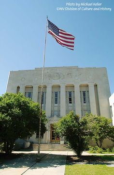 an american flag is flying in front of a white building with trees and bushes around it